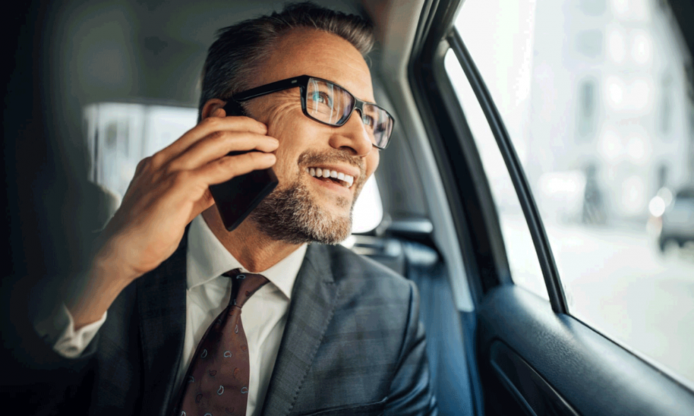 Un hombre de negocios adulto de mediana edad, feliz, sentado en el asiento trasero de un coche, llamando por telefono